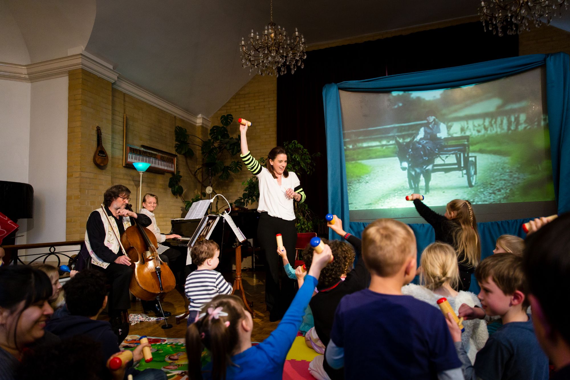 Children waving shakers along with a violinist, cellist and pianist at a family concert in the Recital Hall